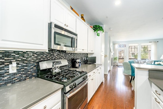 kitchen with tasteful backsplash, open floor plan, wood finished floors, stainless steel appliances, and white cabinetry