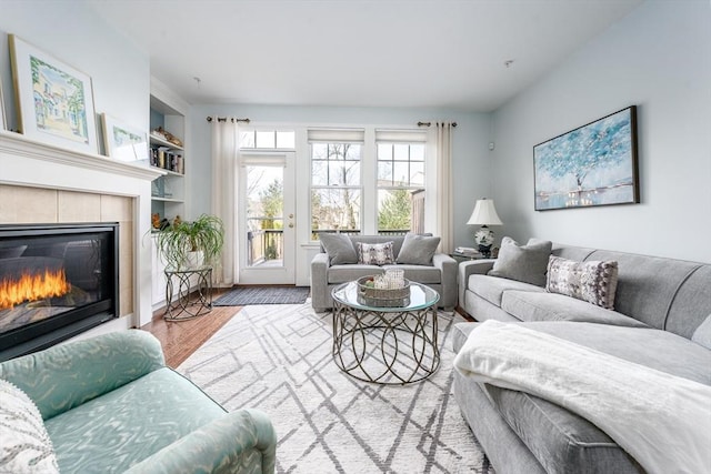 living area with wood finished floors, a tile fireplace, and built in features