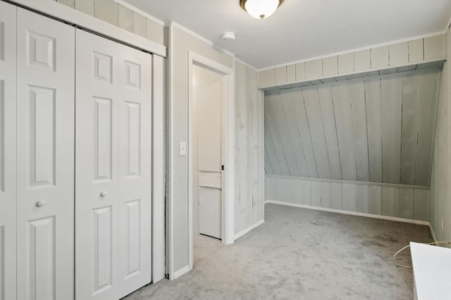 unfurnished bedroom with a closet, ornamental molding, carpet flooring, wooden walls, and baseboards