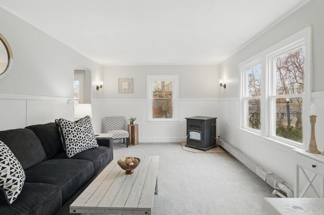 carpeted living room with a wainscoted wall and a wood stove