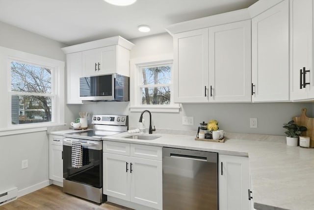 kitchen featuring appliances with stainless steel finishes, a baseboard radiator, a healthy amount of sunlight, and a sink