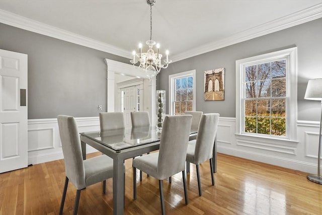 dining area featuring a notable chandelier, a wainscoted wall, light wood-style floors, and ornamental molding