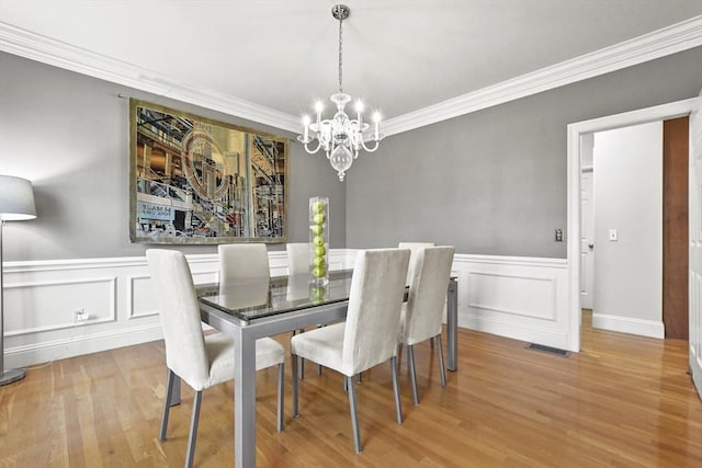 dining room with wood finished floors, visible vents, an inviting chandelier, wainscoting, and crown molding