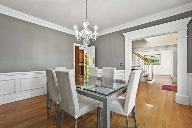 dining area featuring a wainscoted wall, a notable chandelier, wood finished floors, stairway, and crown molding