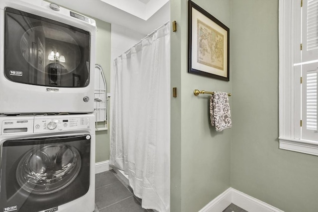 laundry area featuring baseboards, dark tile patterned floors, laundry area, and stacked washing maching and dryer