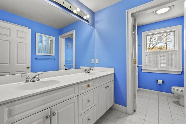 full bathroom with baseboards, double vanity, a sink, tile patterned flooring, and toilet