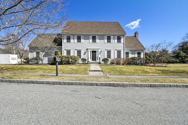 colonial home featuring a chimney and a front lawn