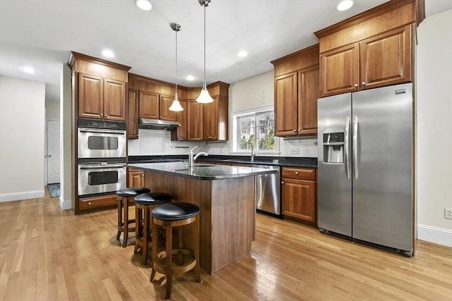 kitchen with under cabinet range hood, backsplash, appliances with stainless steel finishes, and light wood-style flooring