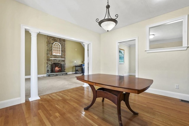 dining room with visible vents, baseboards, decorative columns, a fireplace, and wood finished floors