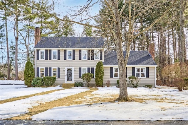 colonial inspired home featuring entry steps, a chimney, and roof with shingles