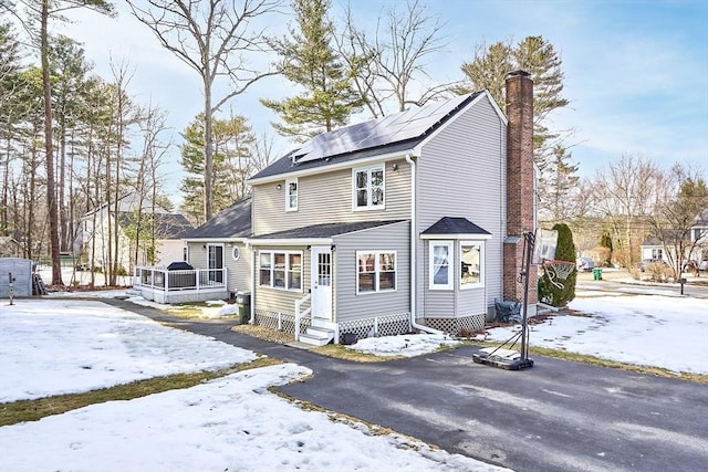 view of front facade featuring entry steps, a chimney, and roof mounted solar panels