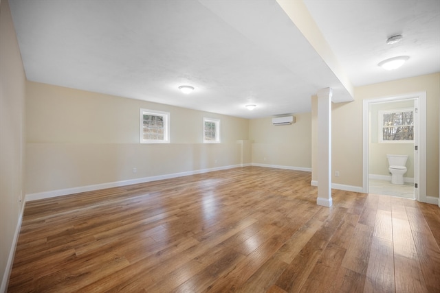 basement with a wall mounted air conditioner, wood-type flooring, and plenty of natural light