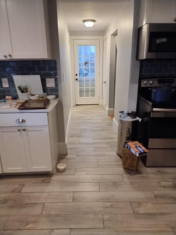 kitchen with tasteful backsplash, black / electric stove, white cabinets, and light hardwood / wood-style floors