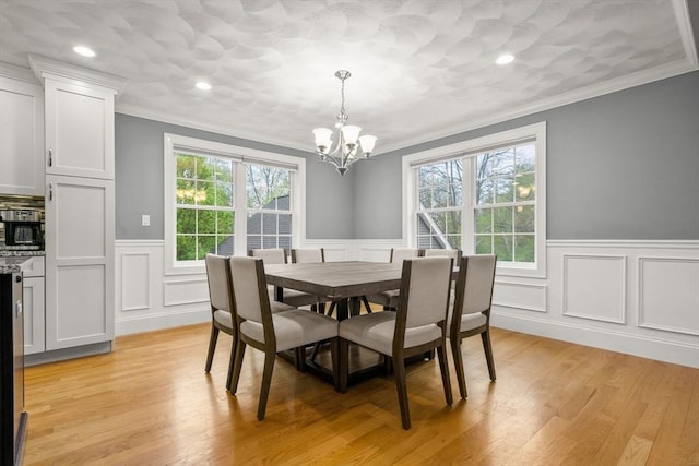 dining area featuring crown molding, a chandelier, a wainscoted wall, plenty of natural light, and a decorative wall