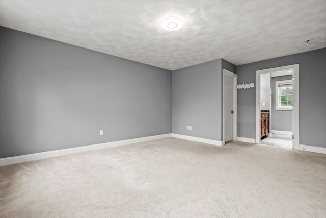 unfurnished bedroom with baseboards, light carpet, a textured ceiling, and ensuite bathroom