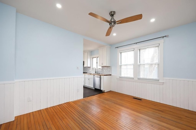 unfurnished room featuring a wainscoted wall, visible vents, dark wood-style flooring, ceiling fan, and a sink