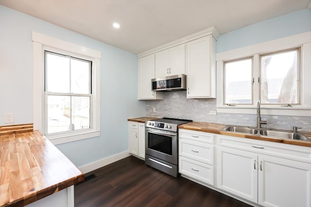 kitchen with backsplash, wooden counters, baseboards, appliances with stainless steel finishes, and a sink