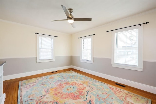 empty room with visible vents, ceiling fan, baseboards, and wood finished floors