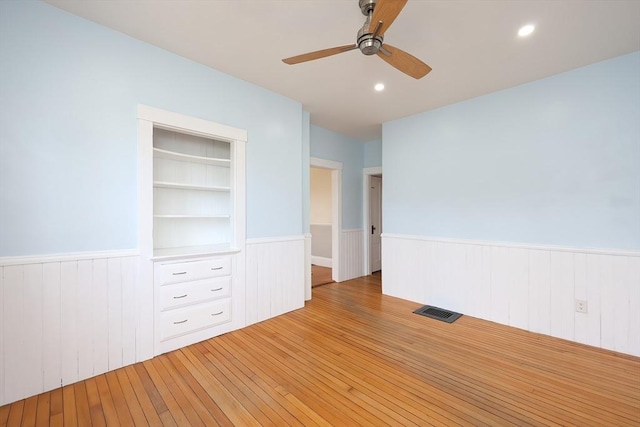 empty room with a wainscoted wall, light wood-style flooring, visible vents, and built in features