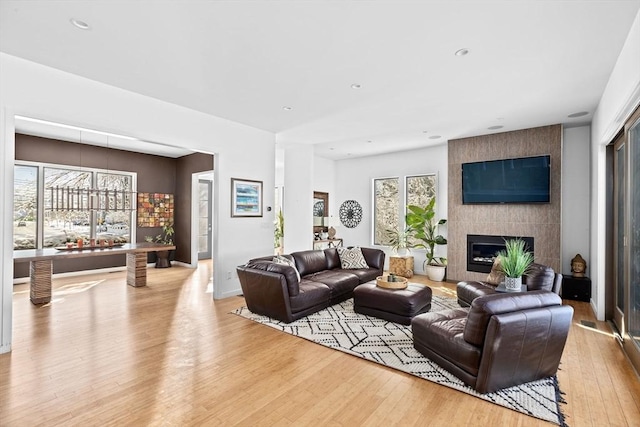 living room featuring a tiled fireplace, a healthy amount of sunlight, and light hardwood / wood-style flooring