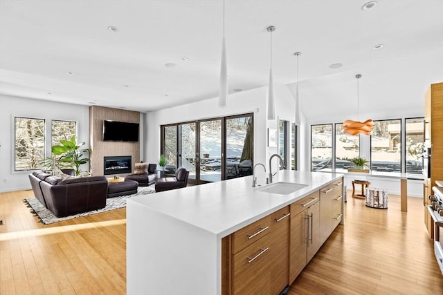 kitchen featuring light hardwood / wood-style flooring, hanging light fixtures, sink, a kitchen island with sink, and a large fireplace