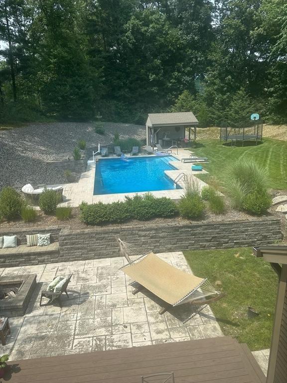 view of swimming pool featuring a patio area, an outbuilding, an outdoor fire pit, a yard, and a trampoline