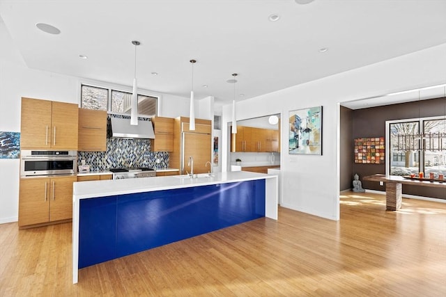 kitchen featuring stainless steel oven, a large island, decorative backsplash, pendant lighting, and wall chimney exhaust hood