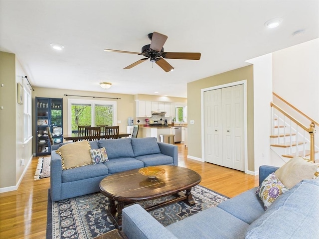 living room featuring stairs, light wood finished floors, a ceiling fan, baseboards, and recessed lighting