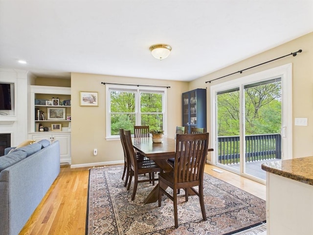 dining area featuring light wood-style floors, healthy amount of natural light, baseboards, and a glass covered fireplace