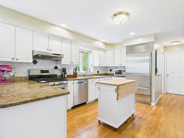 kitchen with stainless steel appliances, under cabinet range hood, a sink, wooden counters, and white cabinetry