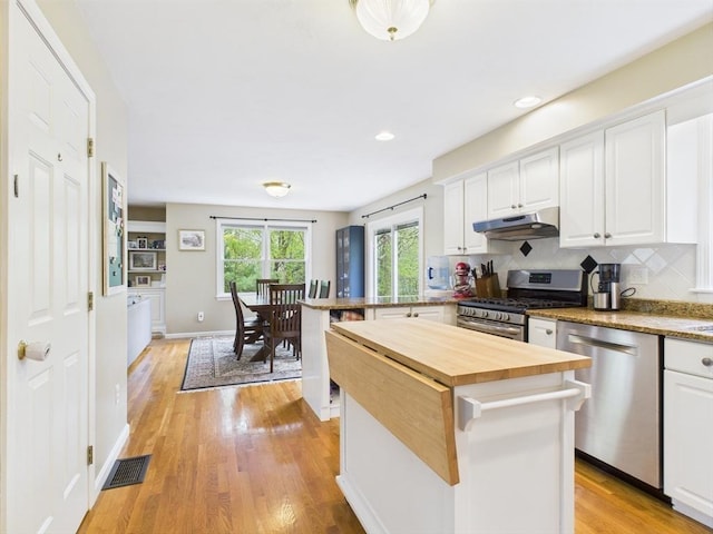 kitchen featuring appliances with stainless steel finishes, butcher block counters, under cabinet range hood, white cabinetry, and light wood-style floors