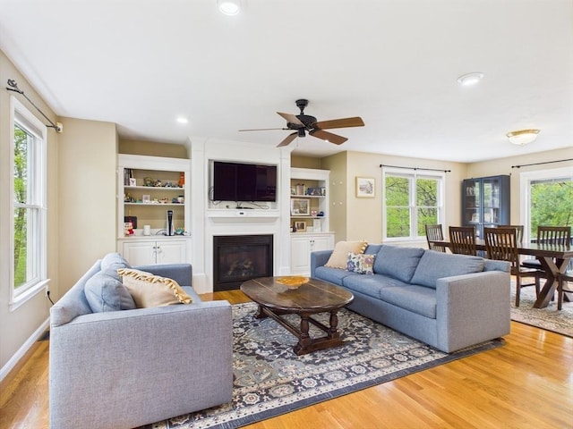 living room featuring healthy amount of natural light, wood finished floors, a ceiling fan, a glass covered fireplace, and recessed lighting