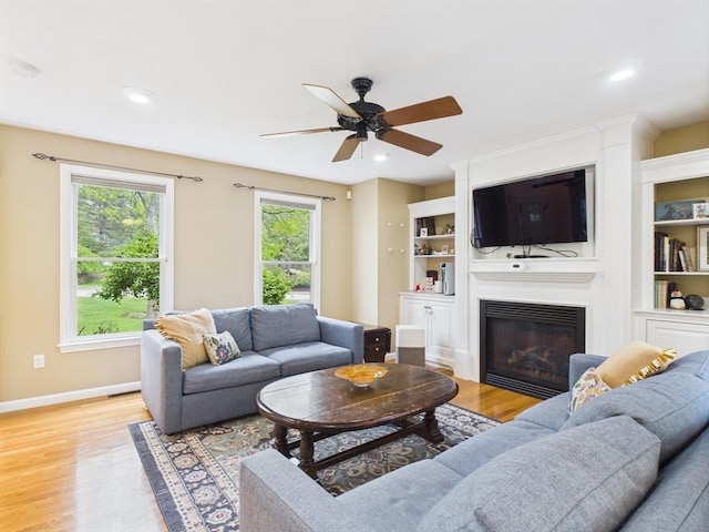 living area with light wood-style floors, a glass covered fireplace, a ceiling fan, baseboards, and recessed lighting