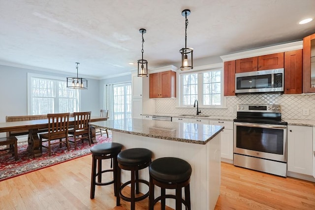 kitchen with stainless steel appliances, crown molding, a sink, and light wood-style flooring