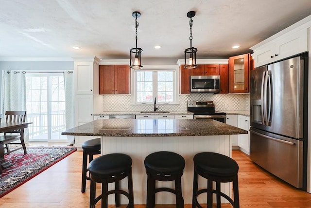 kitchen with a breakfast bar, hanging light fixtures, stainless steel appliances, light wood-style floors, and a sink