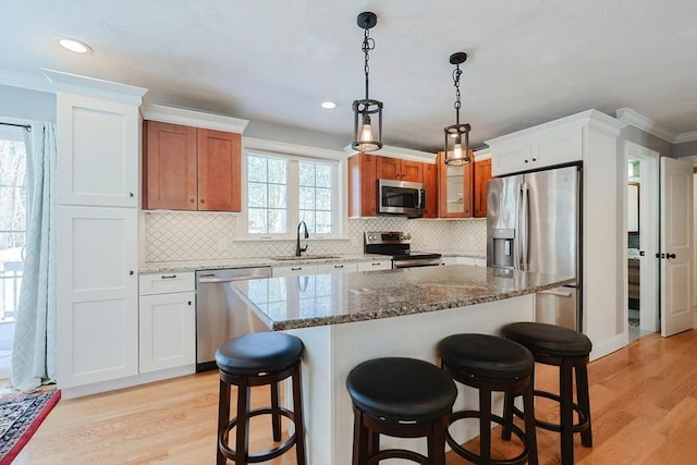 kitchen with appliances with stainless steel finishes, light wood-type flooring, a sink, and a kitchen breakfast bar