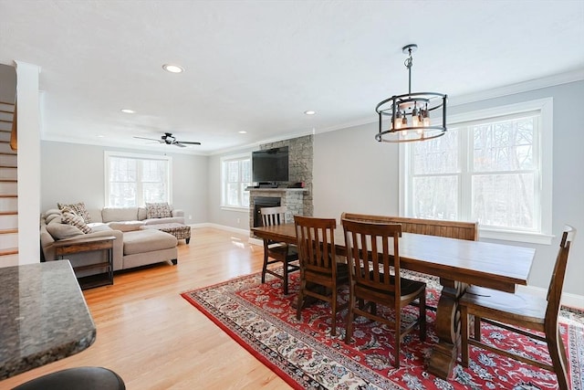 dining space with a fireplace, light wood finished floors, ornamental molding, baseboards, and stairs