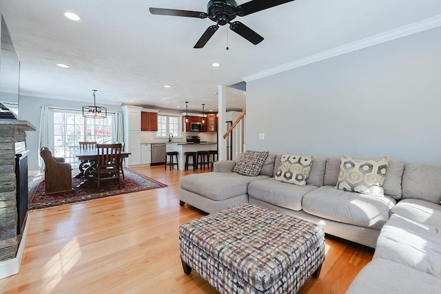 living room with a fireplace, crown molding, light wood finished floors, recessed lighting, and stairs