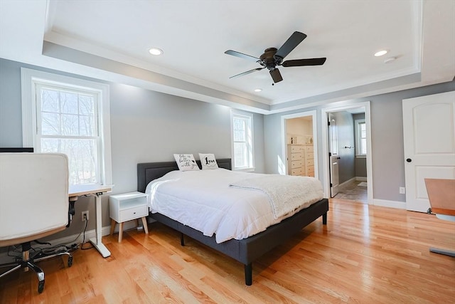 bedroom with light wood-type flooring, baseboards, a raised ceiling, and crown molding