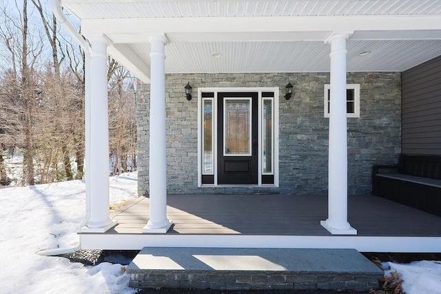 snow covered property entrance featuring covered porch and stone siding