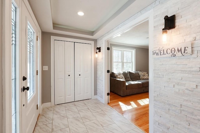 entryway featuring a raised ceiling, crown molding, light wood-style flooring, and baseboards