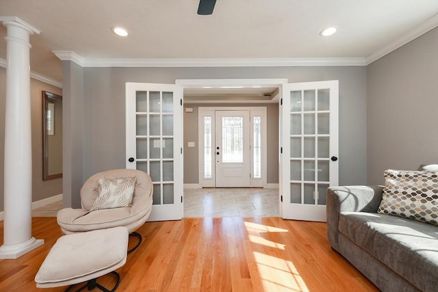 foyer entrance with crown molding, french doors, decorative columns, and light wood finished floors