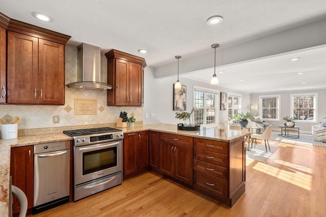 kitchen with decorative light fixtures, kitchen peninsula, wall chimney range hood, stainless steel gas range, and light wood-type flooring