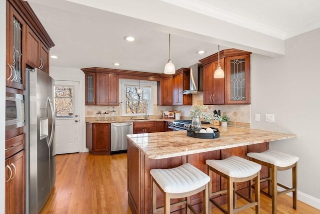 kitchen featuring a breakfast bar area, hanging light fixtures, kitchen peninsula, stainless steel appliances, and wall chimney range hood