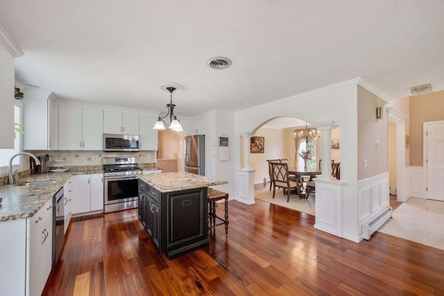 kitchen featuring appliances with stainless steel finishes, a sink, arched walkways, a baseboard heating unit, and white cabinetry