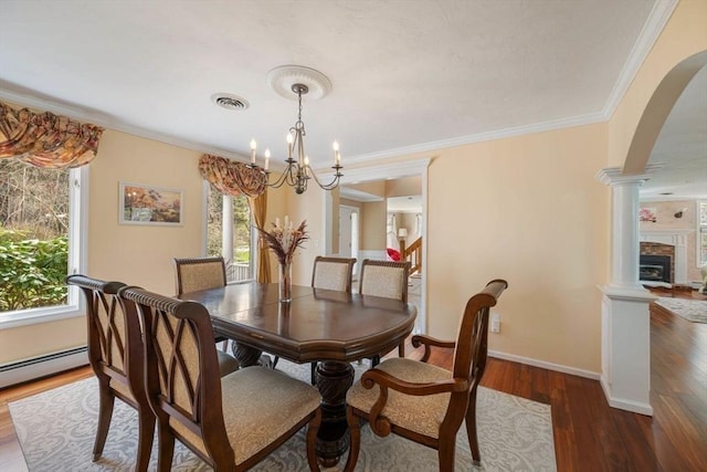 dining room with arched walkways, plenty of natural light, ornate columns, wood finished floors, and ornamental molding