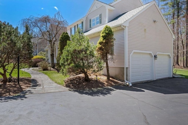 view of home's exterior with a garage, asphalt driveway, and roof with shingles