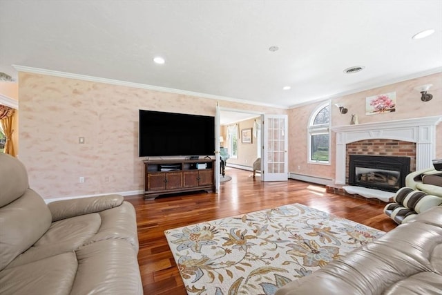 living room with a baseboard heating unit, ornamental molding, wood finished floors, baseboards, and a brick fireplace