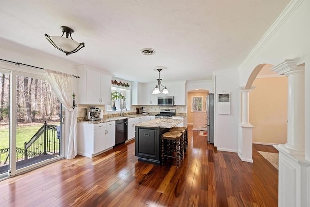 kitchen featuring stainless steel appliances, decorative columns, arched walkways, white cabinets, and ornamental molding