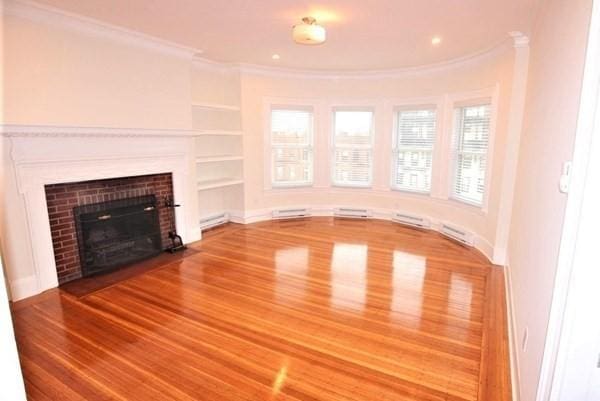 unfurnished living room with ornamental molding, wood finished floors, a baseboard radiator, a fireplace with flush hearth, and baseboards